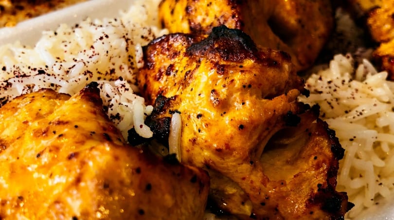 Close-up of golden-brown grilled chicken pieces with white rice, sprinkled with dark spices.