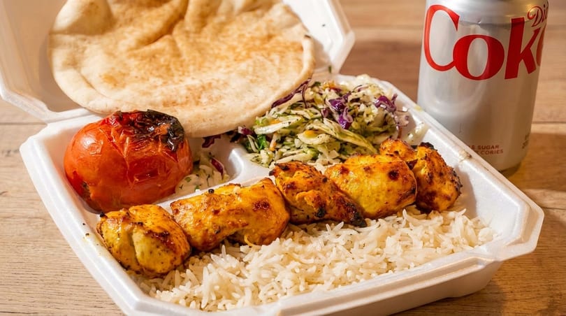 Chicken shish tawook, rice, pita, grilled tomato, coleslaw, and a Diet Coke in a takeout container.